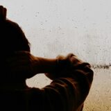 雨の窓辺に立つ男性