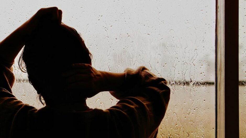 雨の窓辺に立つ男性