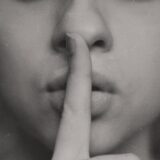 指を口に当てて「秘密」を示すポーズ — gatekeep(情報を独占して教えない)のアイキャッチ