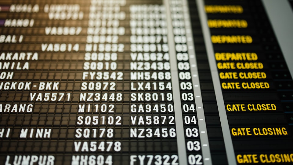 空港の発着案内ボードと旅行者のイメージ