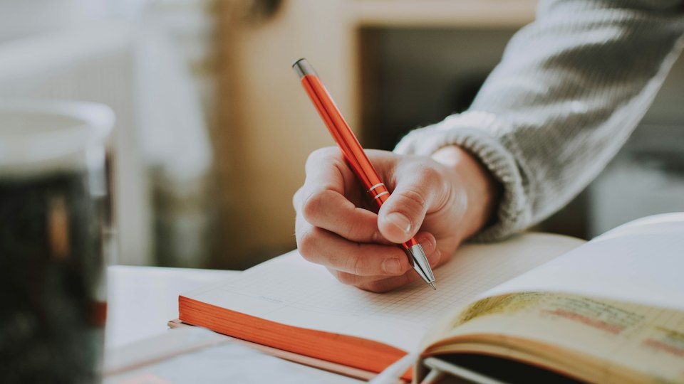 赤いペンで本に書き込む人の手