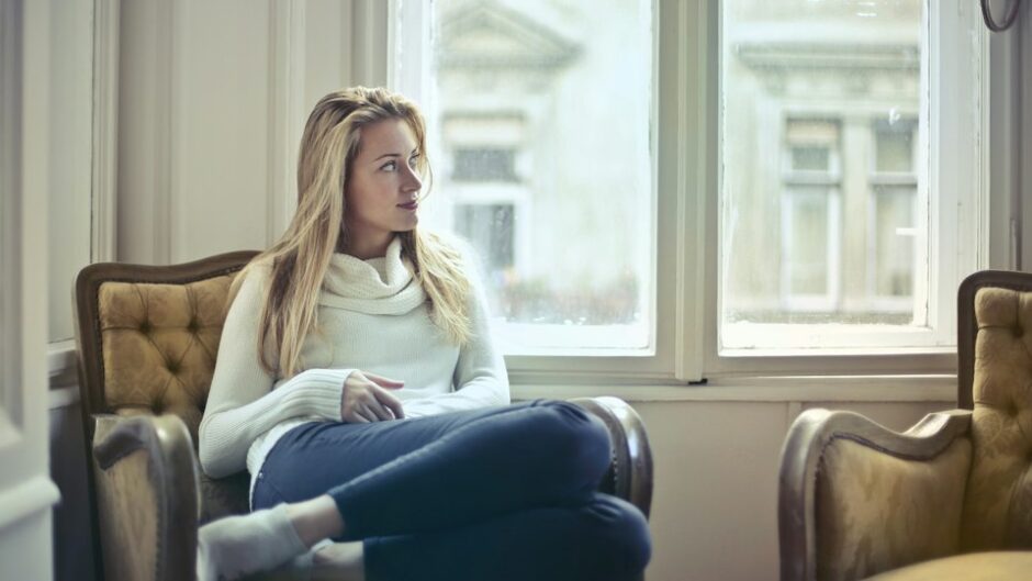 窓の前で考え込むように外を見つめる女性