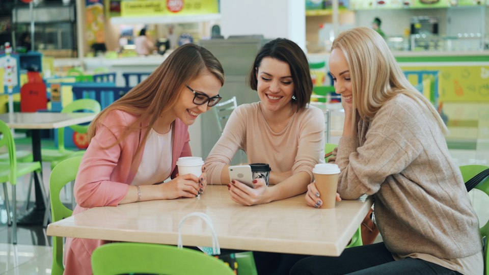カフェでスマホを見ながら笑い合う女性たち