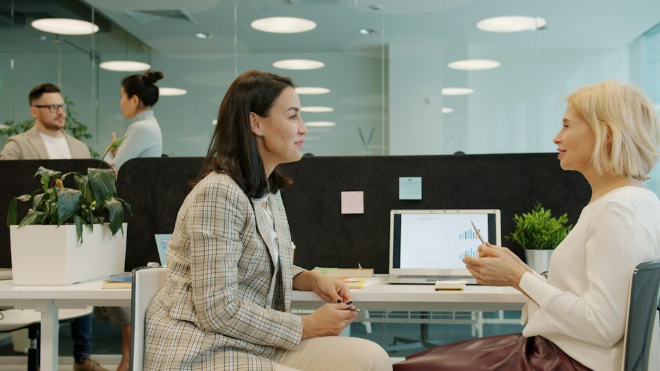 オフィスでノートパソコンを見ながら楽しそうに話す同僚の女性たち