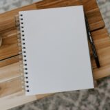 木のベンチの上に置かれた白紙のノートとペン